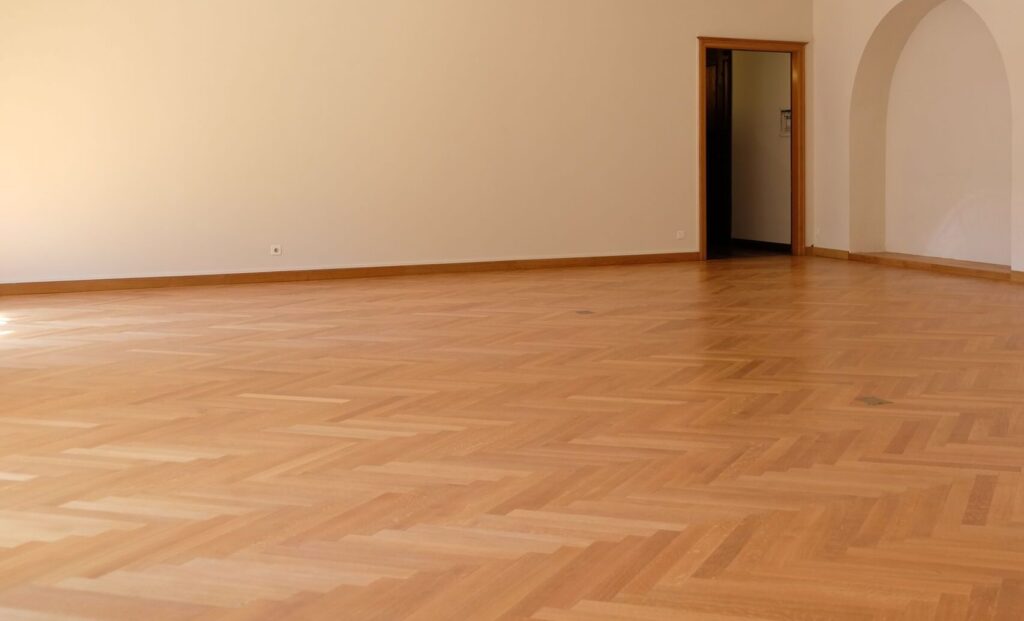 A large empty room with elegant wooden flooring, arches, and natural lighting, perfect for interior design inspiration.